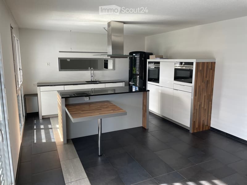 Modern kitchen with white cabinets, dark countertops, stainless steel appliances, and a wooden island with a built-in sink and seating area.
