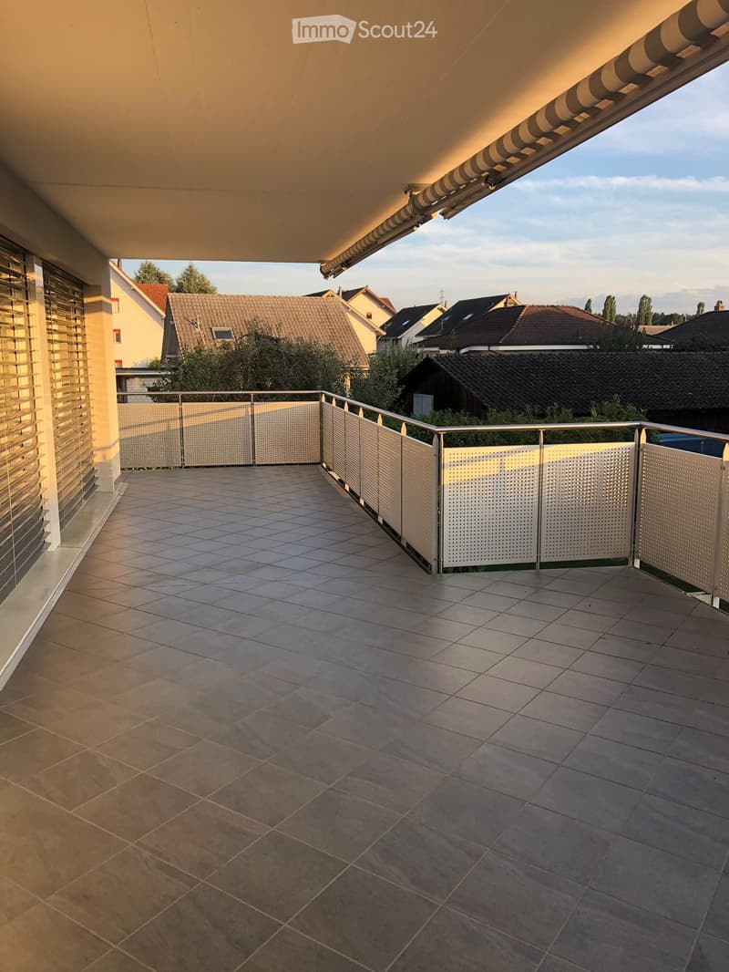 Balcony with tiled floor, metal railing, and a retractable awning, overlooking a residential area with houses and trees.