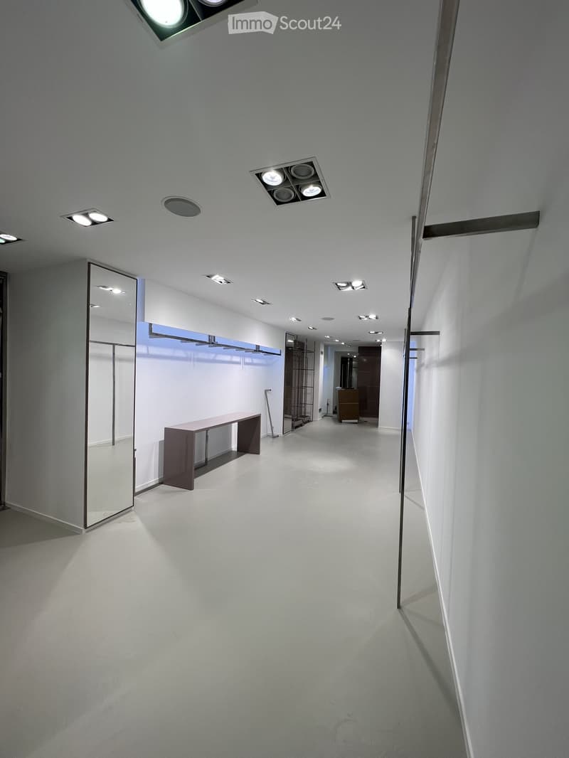 Modern, minimalist hallway with white walls, recessed lighting, and a sleek bench on the left side.