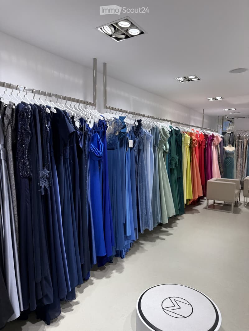 A well-lit clothing store with racks of dresses in various colors, a small seating area with a chair, and a round table with a logo.