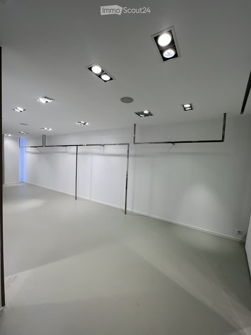 Empty room with white walls, grey floor, and recessed ceiling lights. No furniture or equipment present.
