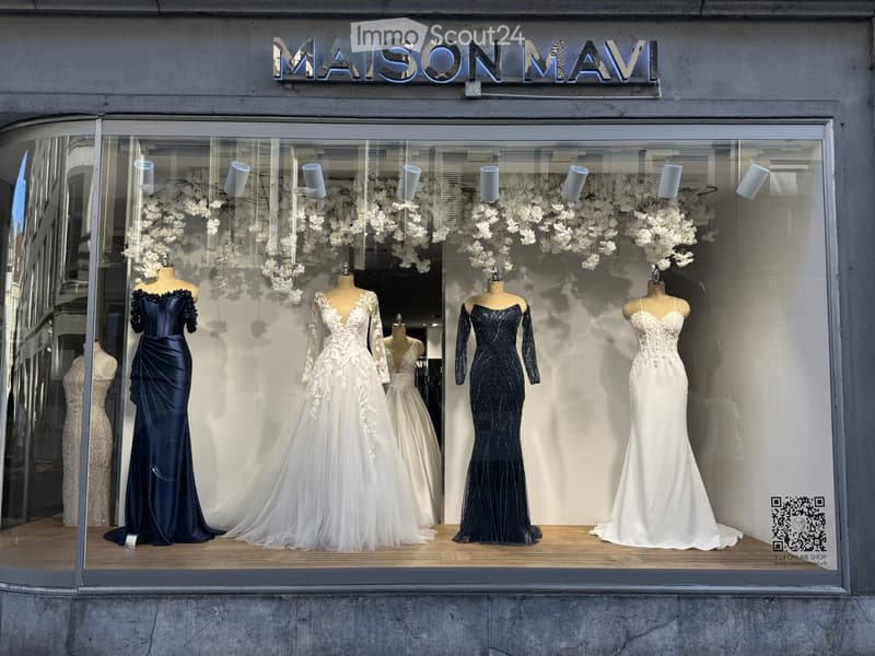 Storefront display with five wedding dresses on mannequins, surrounded by white floral decorations.