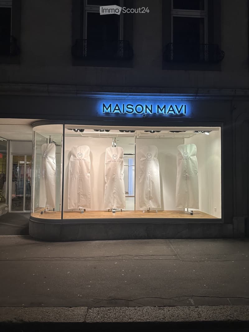 Storefront with large glass windows displaying white garments on mannequins, illuminated sign reading "MAISON MAVI" above the entrance.