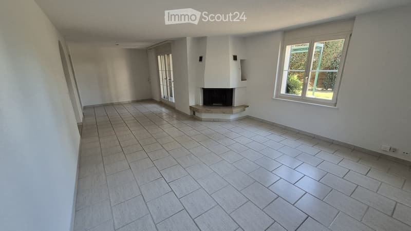 Empty room with tiled floor, white walls, fireplace, large window, and glass door leading outside.