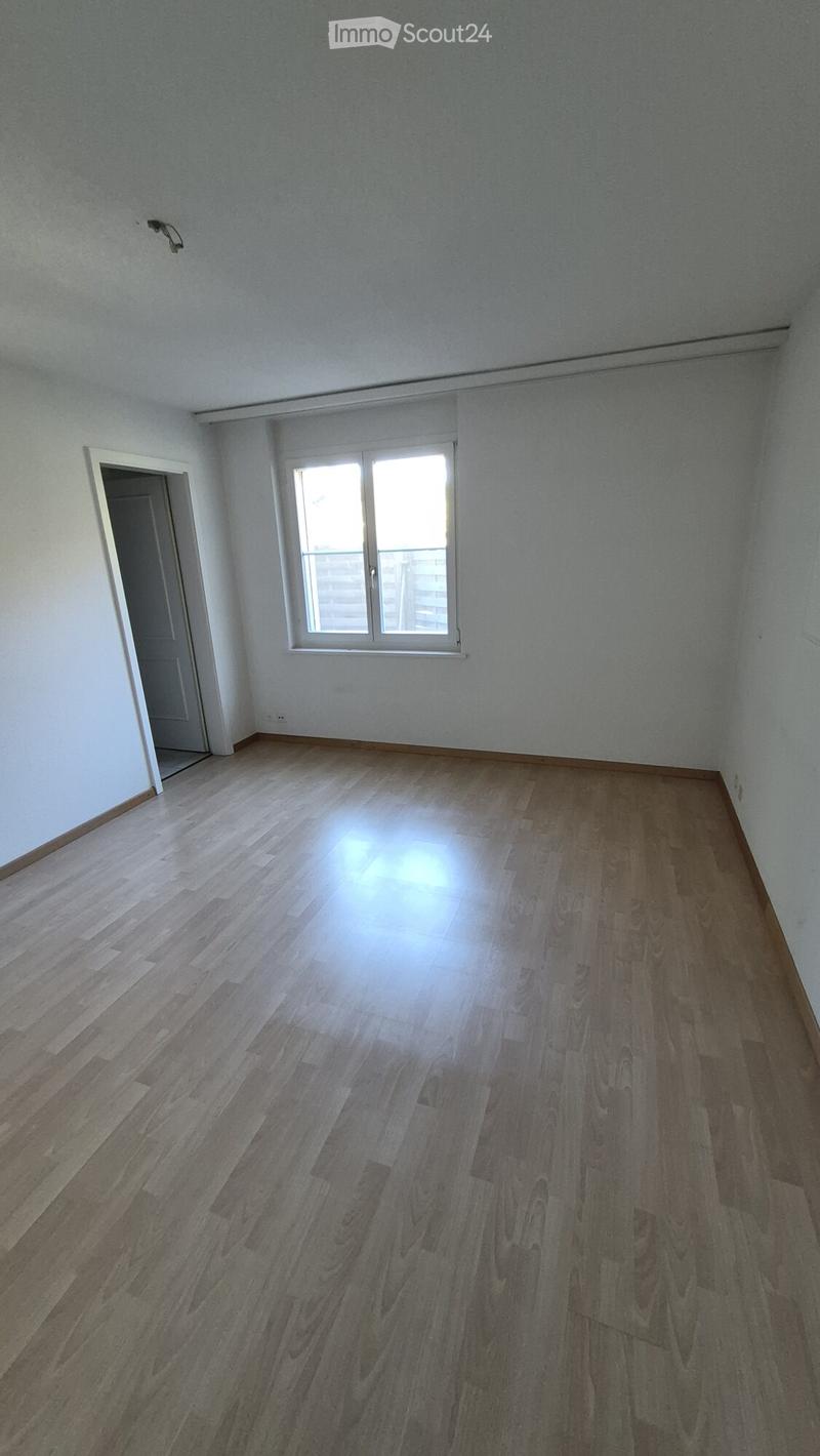 Empty room with wooden flooring, white walls, and a window with blinds. There is a doorway leading to another room.