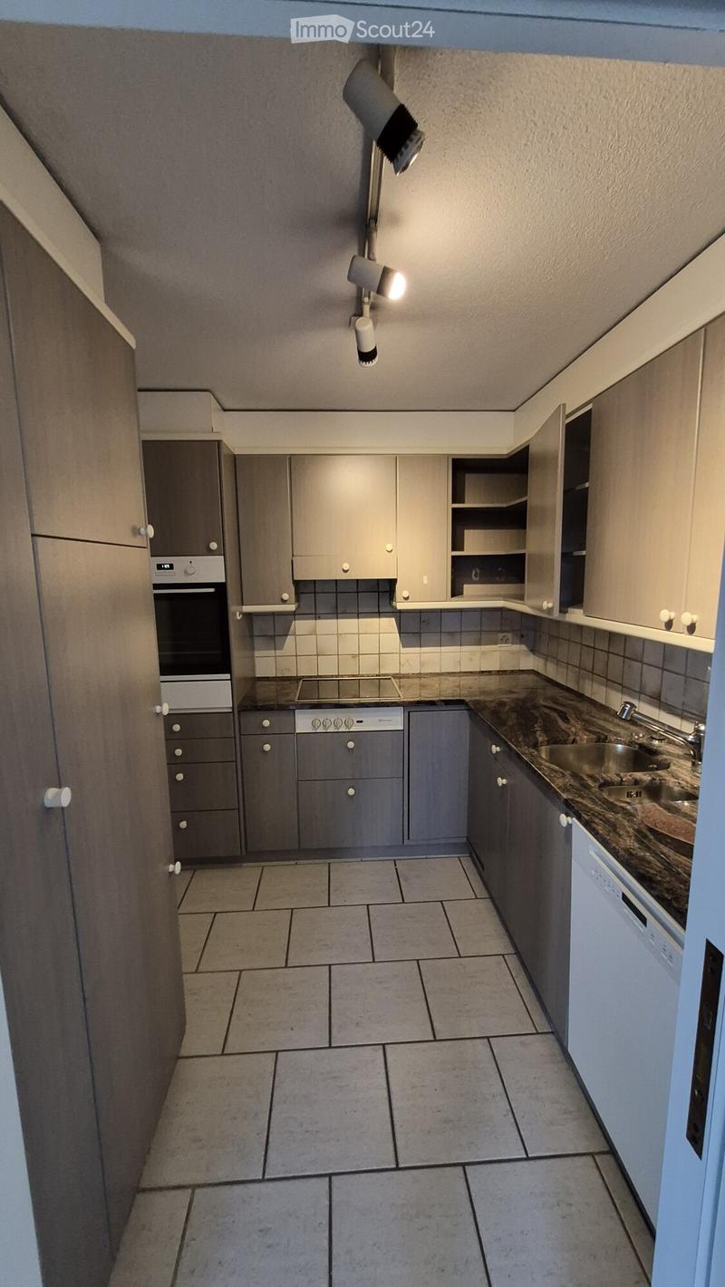 Modern kitchen with grey cabinets, tiled walls, and a marble countertop. Features an oven, dishwasher, and sink.
