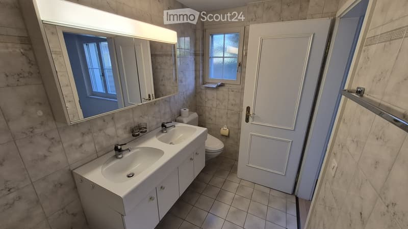 Modern bathroom with double sink, large mirror, toilet, and tiled walls and floor.