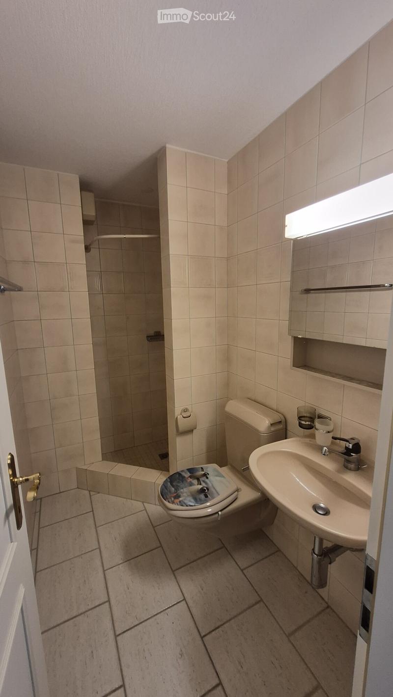 Small bathroom with beige tiled walls and floor, featuring a toilet, sink, and shower area.