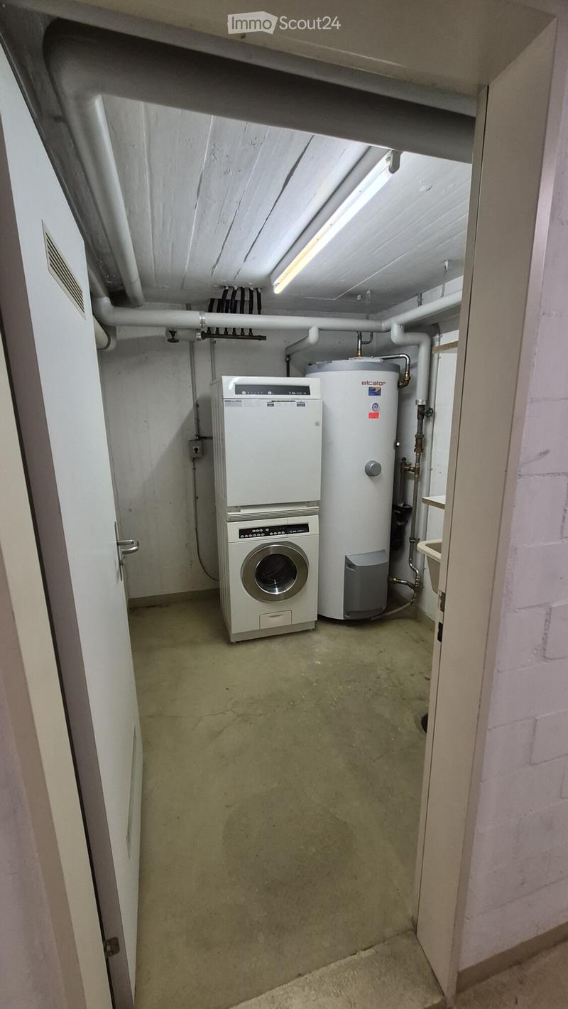 Utility room with a washing machine and water heater, exposed pipes, and a concrete floor.