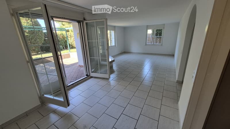 Empty room with tiled floor, large sliding glass doors leading to an outdoor area, and two windows on the far wall.