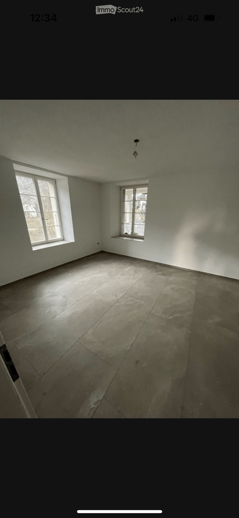 Empty room with bare walls and a concrete floor, featuring two windows allowing natural light to enter.