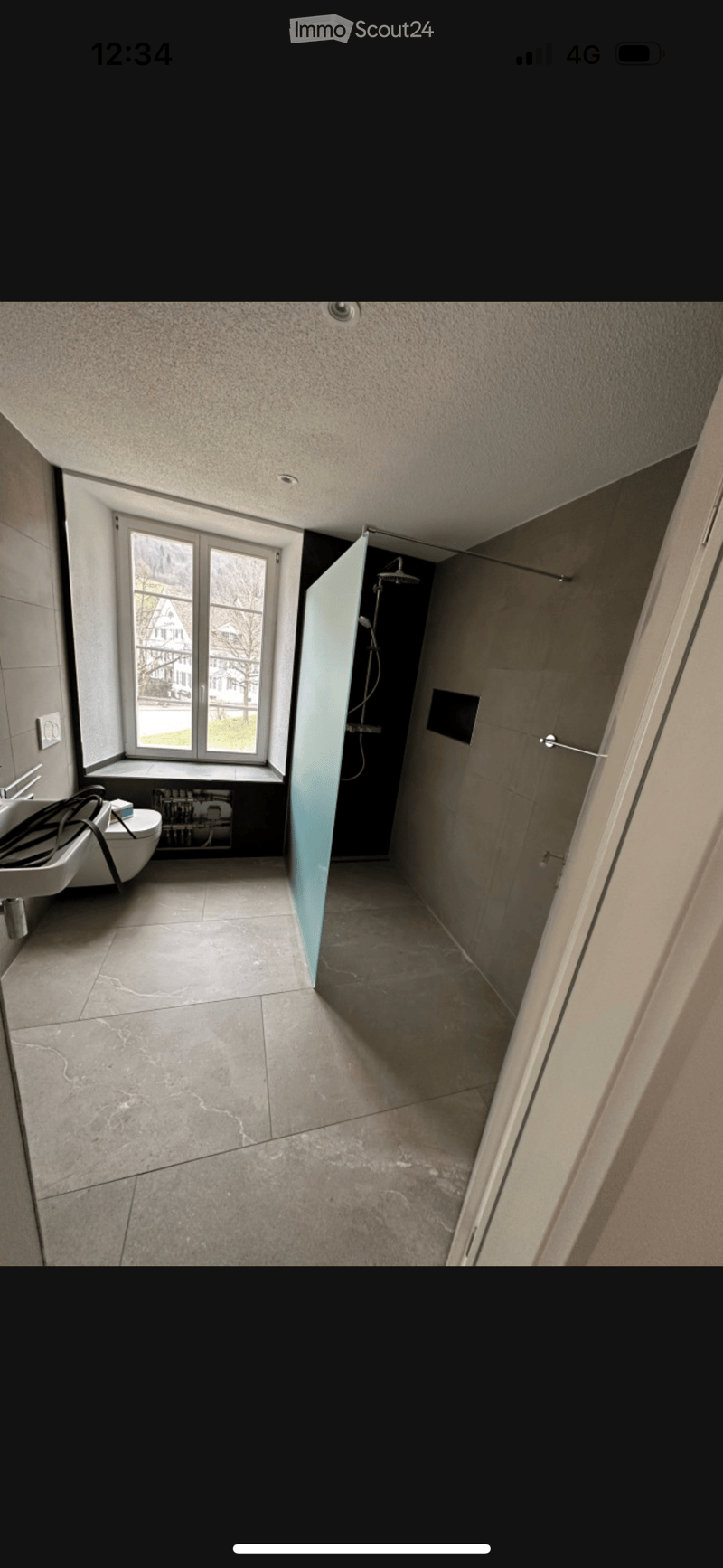 Modern bathroom with tiled floor, large window, sink, toilet, and separate shower area with glass door.