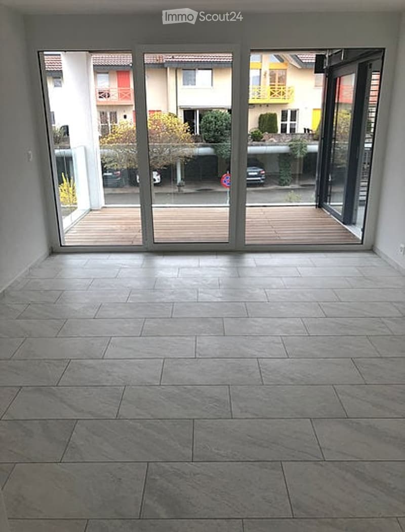 Empty room with large sliding glass doors leading to a wooden deck, tiled floor, and view of neighboring buildings.