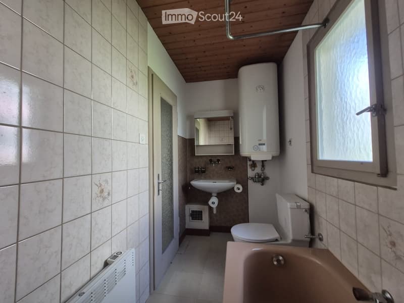 Compact bathroom with tiled walls, a toilet, sink, bathtub, and a water heater. Features a wooden ceiling and a window for natural light.