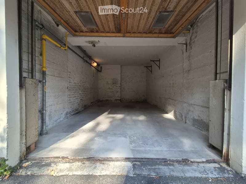 Empty garage with exposed brick walls, concrete floor, wooden ceiling, and industrial-style lighting.