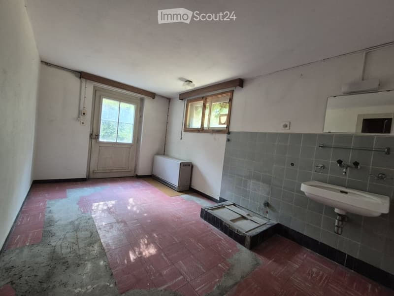 Empty bathroom with tiled walls, a sink, a mirror, a window, and a door leading outside. The floor has a mix of red tiles and concrete.
