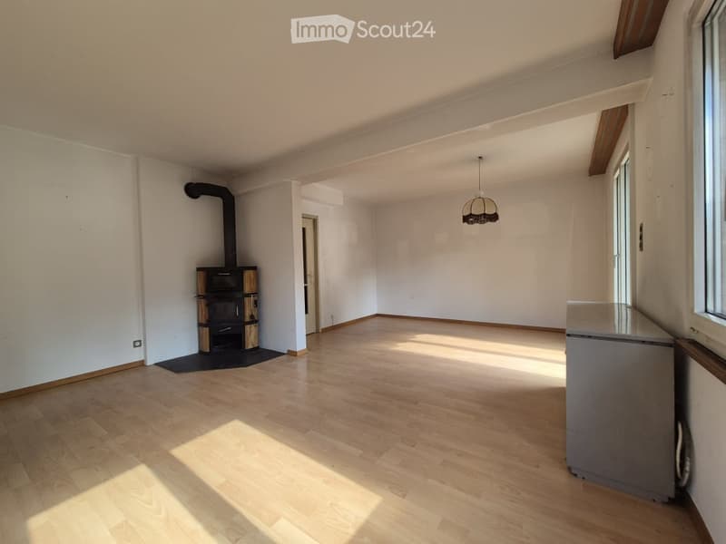 Empty room with wooden flooring, white walls, and a fireplace. Natural light streams in from a window on the right side.