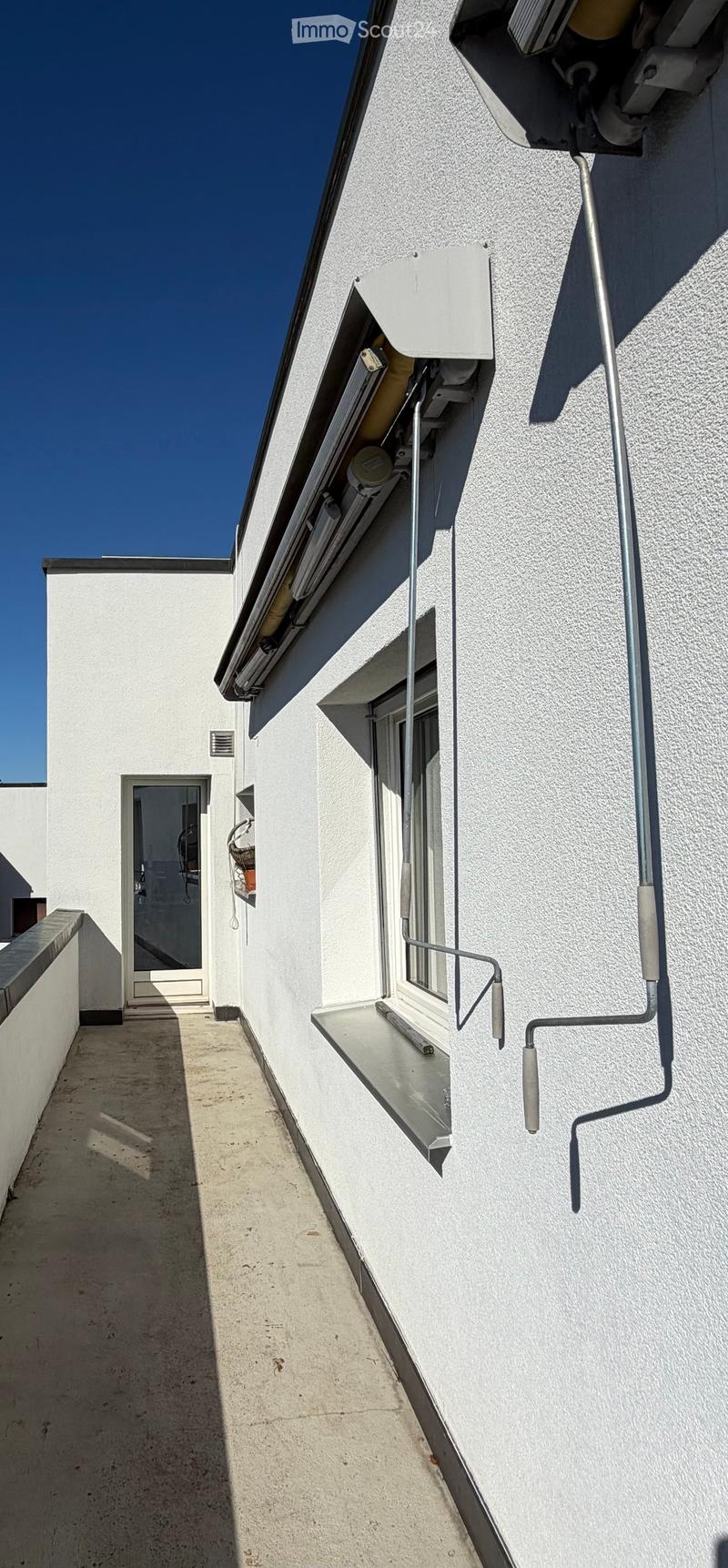 Narrow balcony with white walls, a window with a small shelf, and a door leading to another area.