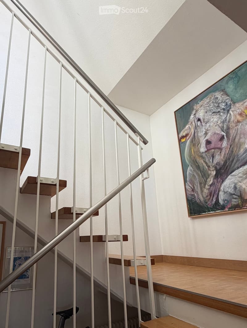 Modern staircase with wooden steps, metal railing, and a large painting of a cow on the wall.