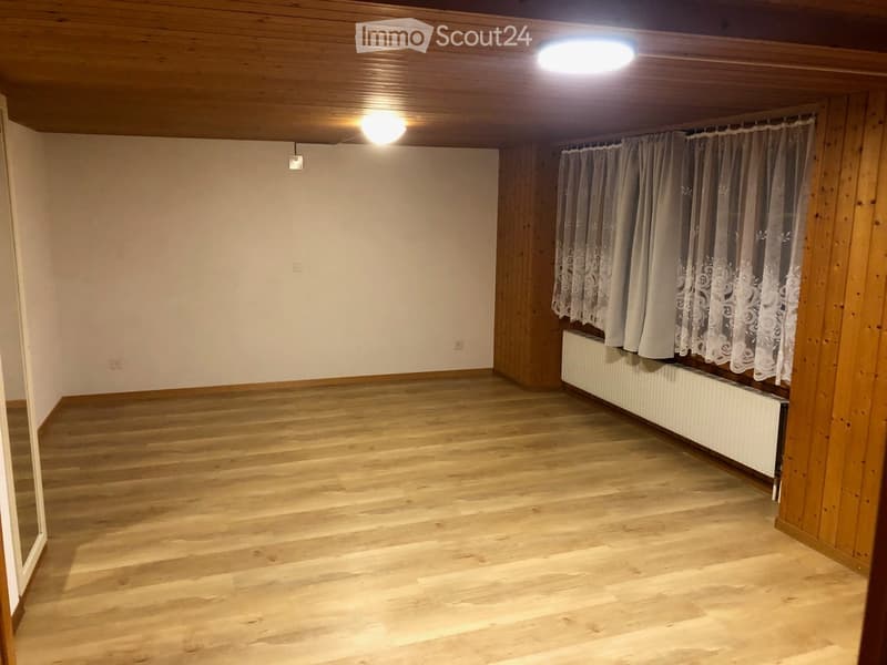 Empty room with wooden flooring, white walls, and a radiator under a window with curtains.