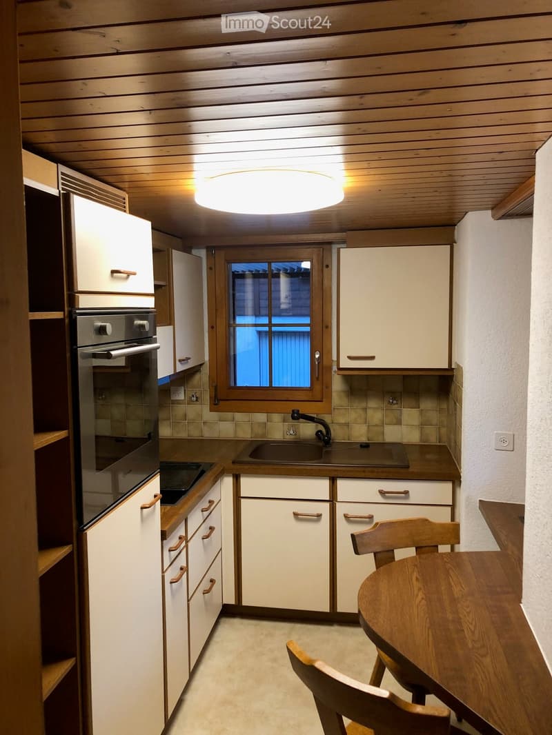 Compact kitchen with white cabinets, wooden accents, a sink, oven, and a small dining area with a table and chairs.