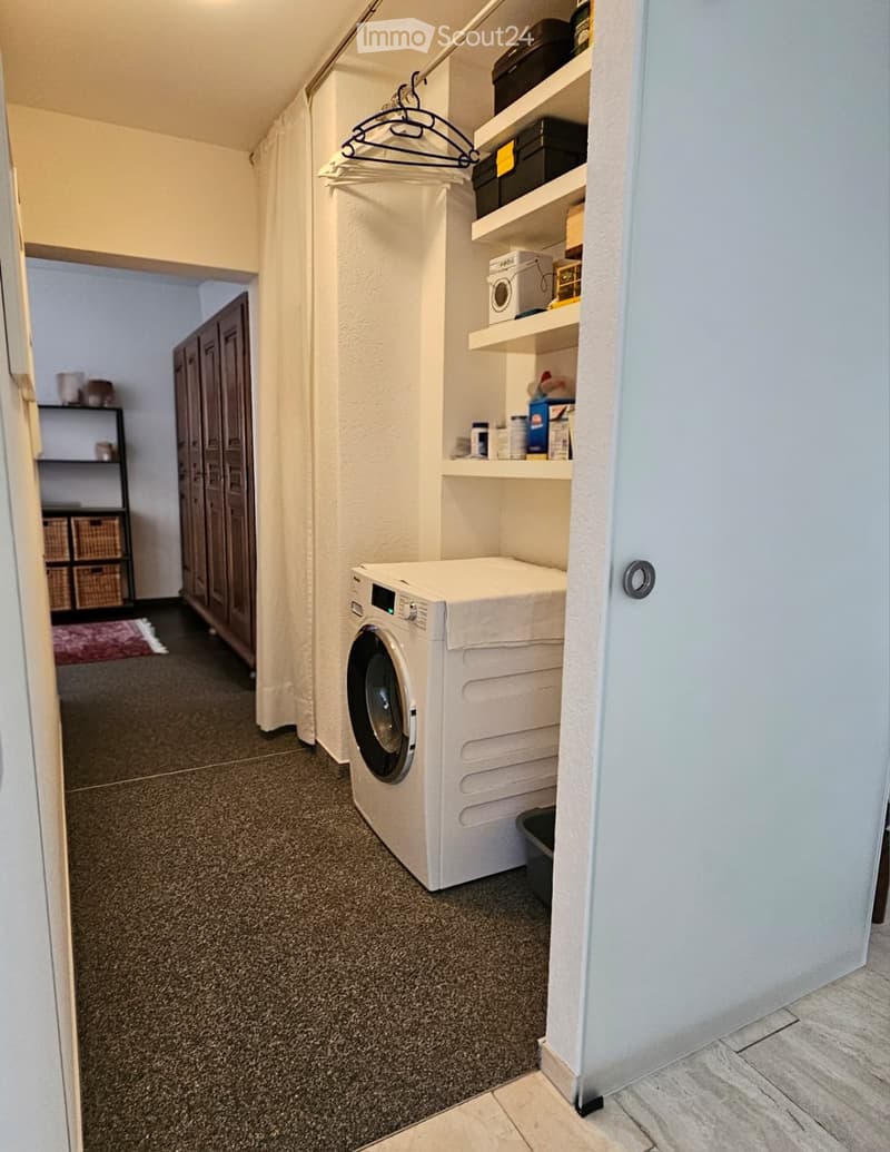 A small, well-organized laundry area with a white washing machine, built-in shelves, and a hanging rod for clothes.