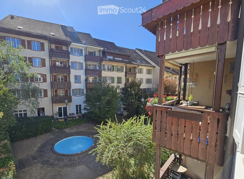 Courtyard with a small swimming pool, surrounded by greenery and buildings with balconies and windows.