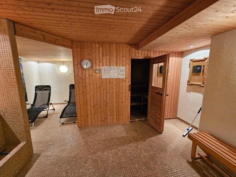 Wooden sauna room with tiled floor, two black chairs, a wooden bench, a mirror, and a clock on the wall.
