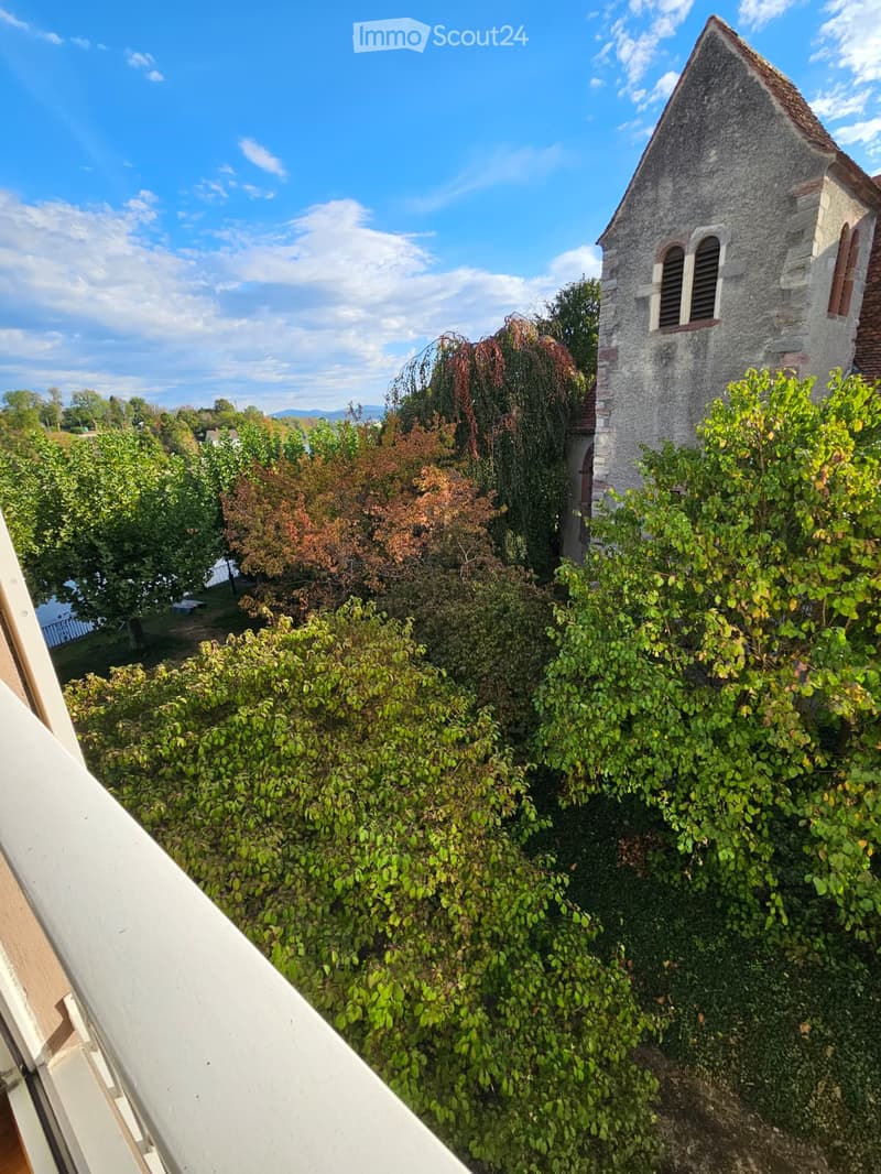 View from a balcony overlooking a lush garden area with a stone tower and trees in the background.