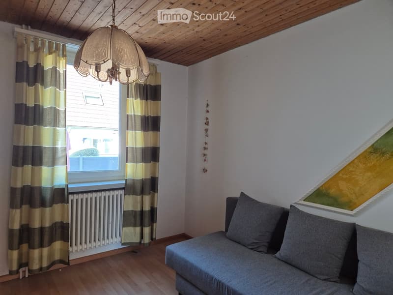 Living room with wooden floor, grey sofa, pendant light, striped curtains, radiator, and a painting on the wall.