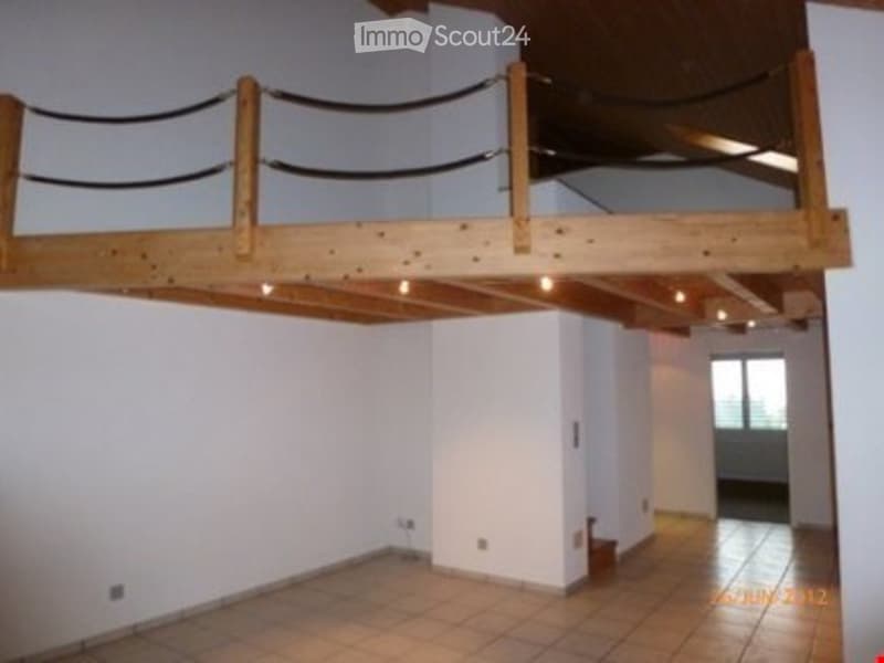 Empty room with tiled floor, white walls, and a wooden loft area with a railing above.