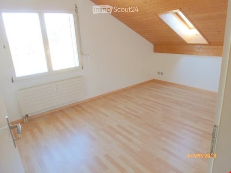 Empty room with wooden flooring, white walls, large window, radiator, and skylight in the ceiling.