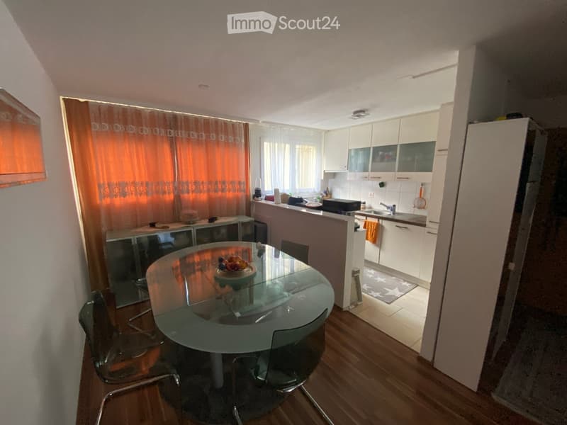 A modern kitchen and dining area with a glass dining table, chairs, white cabinets, and a sink.