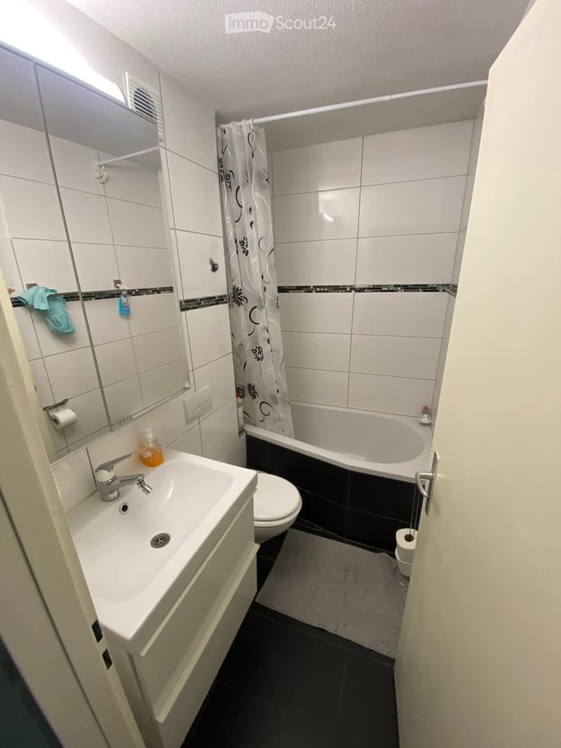 Modern bathroom with white tiles, a sink with a faucet, a toilet, a bathtub with a shower curtain, and a mirror above the sink.