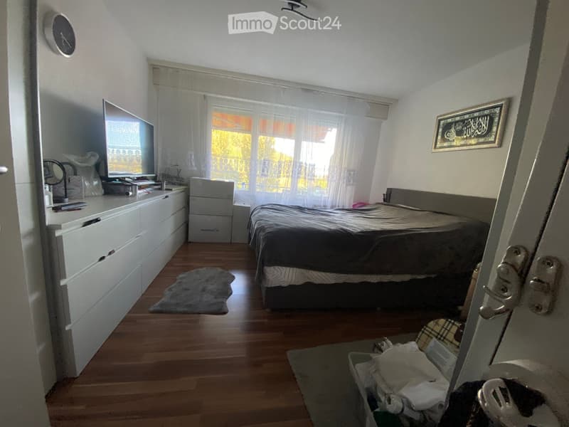 Bedroom with a bed, nightstand, mirror, screen, chair, table, and framed picture. Wooden floor and white walls.