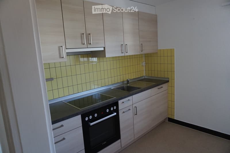 Modern kitchen with light wood cabinets, stainless steel sink, built-in oven, and stove. Yellow tiled backsplash and gray countertops.