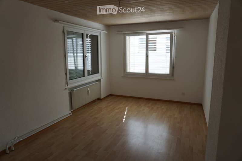 Empty room with wooden flooring, white walls, two windows with blinds, and a radiator under one window.