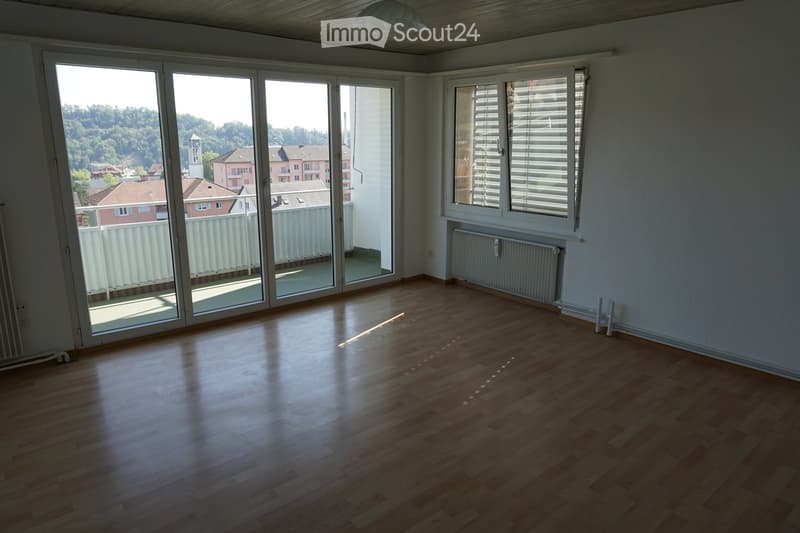 Empty room with wooden flooring, large sliding glass doors leading to a balcony, and a radiator on the wall.