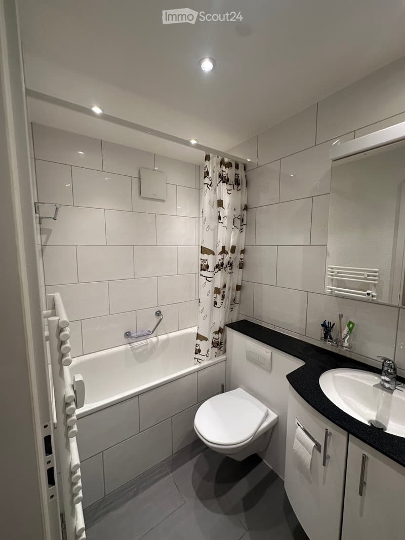 Modern bathroom with white tiles, bathtub, toilet, sink, and a shower curtain with owl designs.