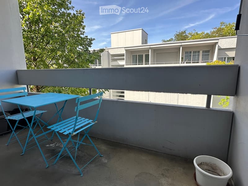Balcony with a blue table and two matching chairs, overlooking a modern building with balconies.