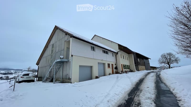 Two-story house with white siding, garage, and balcony, surrounded by snow-covered ground and trees.