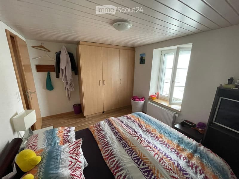 Bedroom with a bed, colorful bedspread, nightstand, wardrobe, and a window with a view.