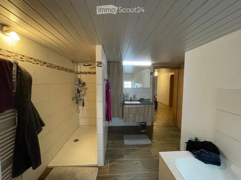 Modern bathroom with a walk-in shower, sink, mirror, and wooden flooring. Includes towels, a bathrobe, and a bathmat.