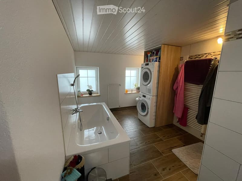 Bathroom with a bathtub, shower, washing machine, radiator, mirror, cabinet, towel rack, and a small stool.
