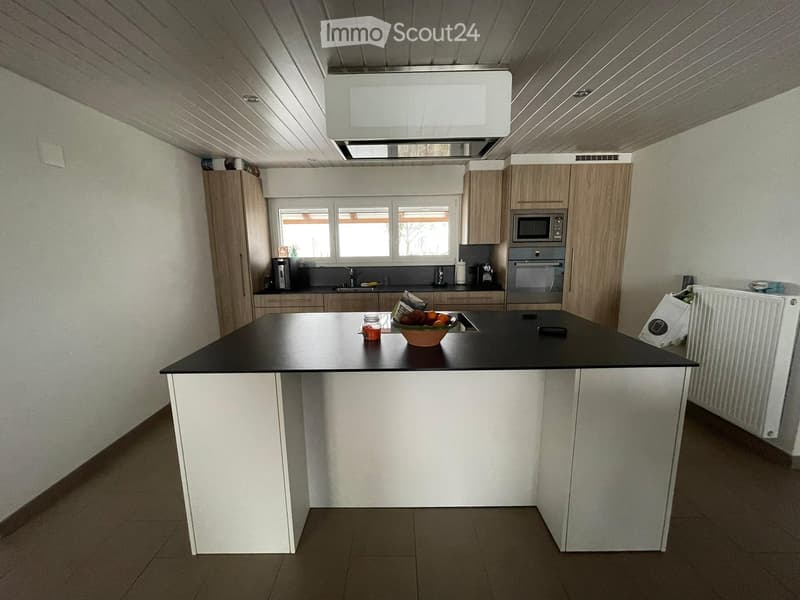 Modern kitchen with white cabinets, a black countertop island, and stainless steel appliances including a microwave and oven. The island features a bowl of fruit and a jar on the countertop.