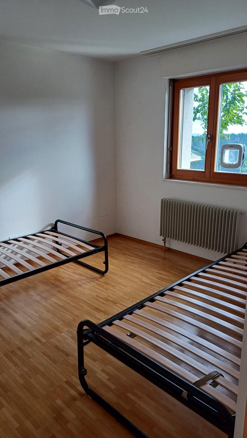 Empty bedroom with wooden floor, white walls, and a single bed frame against the wall.