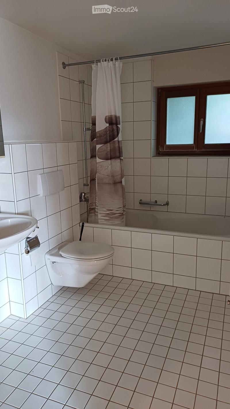 Modern bathroom with white tiles, a toilet, a sink, a bathtub, a shower curtain, and a handrail.