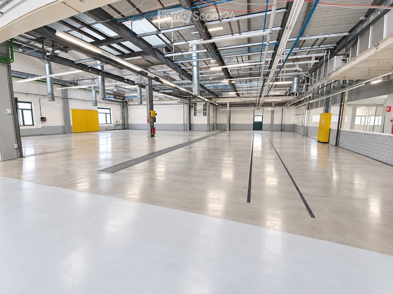 Large, empty industrial-style room with concrete floors, exposed metal beams, and large windows. No furniture or equipment is present.