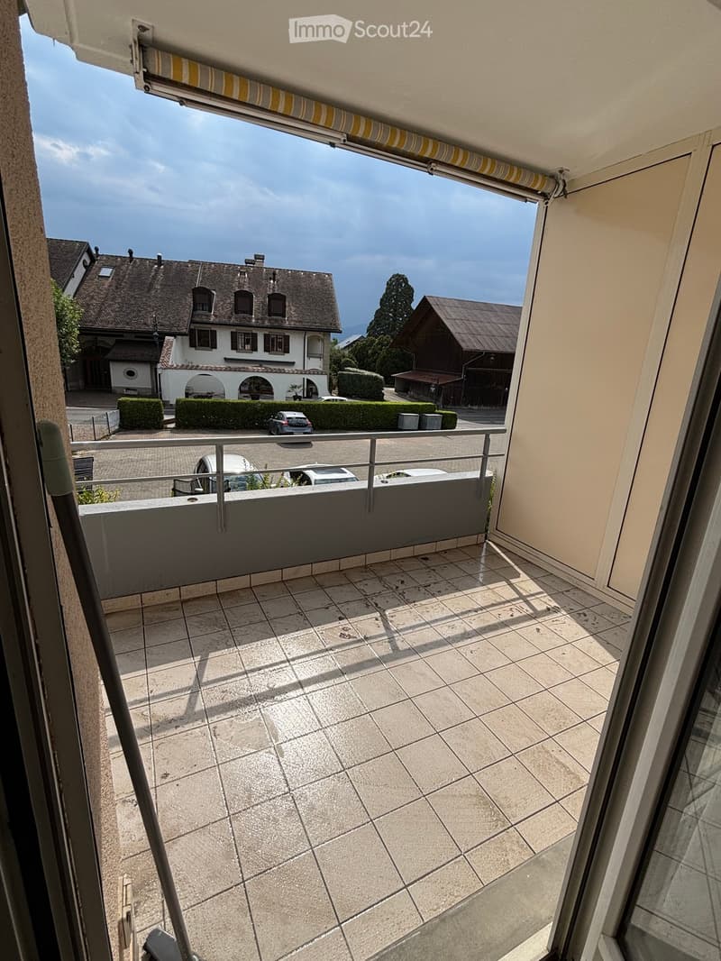 Balcony with tiled floor, metal railing, and view of surrounding houses and greenery.