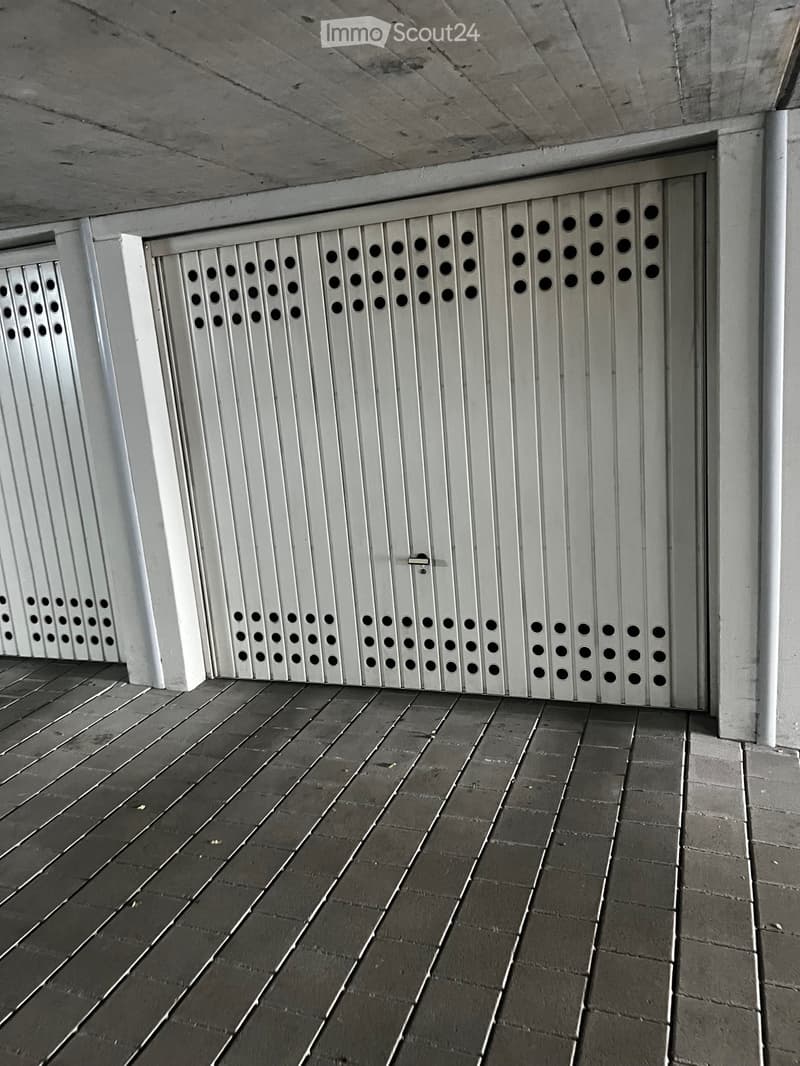 A concrete corridor with a raised ground floor, featuring a white metal gate with circular perforations and a tiled floor.